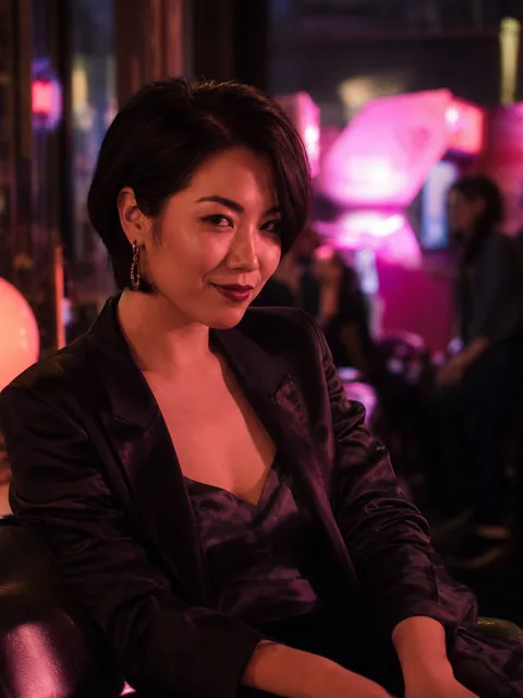 Jade, an adult woman in a black satin jacket at a neon lit arcade bar