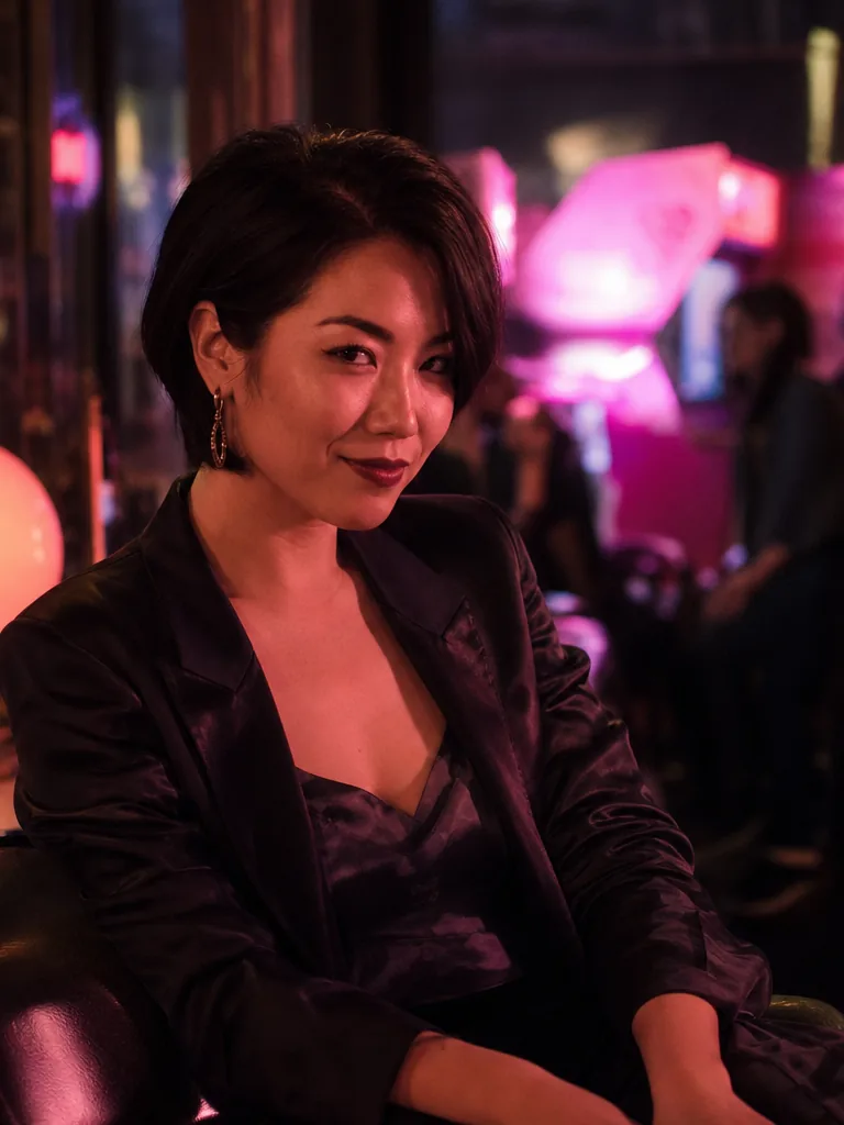 Jade, an adult woman in a black satin jacket at a neon lit arcade bar